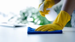 Cleaning professional disinfecting office table surfaces with spray and cloth to maintain a sanitary workspace