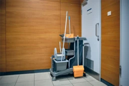 Janitorial cleaning cart stocked with supplies, including mops, buckets, and cleaning tools, positioned in a commercial or airport facility corridor